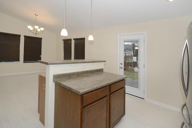 kitchen featuring baseboards, lofted ceiling, a kitchen island, freestanding refrigerator, and hanging light fixtures