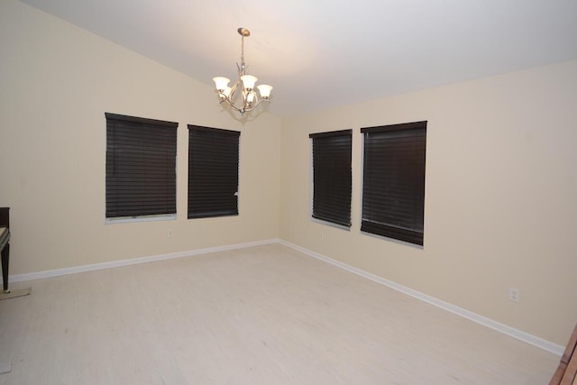 spare room featuring light wood-style floors, a chandelier, and baseboards