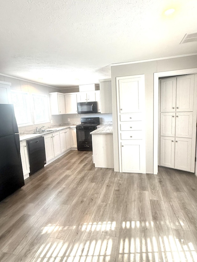 kitchen featuring a textured ceiling, light wood-style flooring, a sink, light countertops, and black appliances