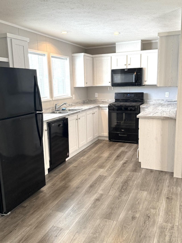 kitchen with a textured ceiling, a sink, light countertops, light wood-type flooring, and black appliances