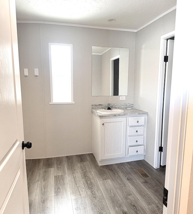 bathroom with wood finished floors, visible vents, and crown molding