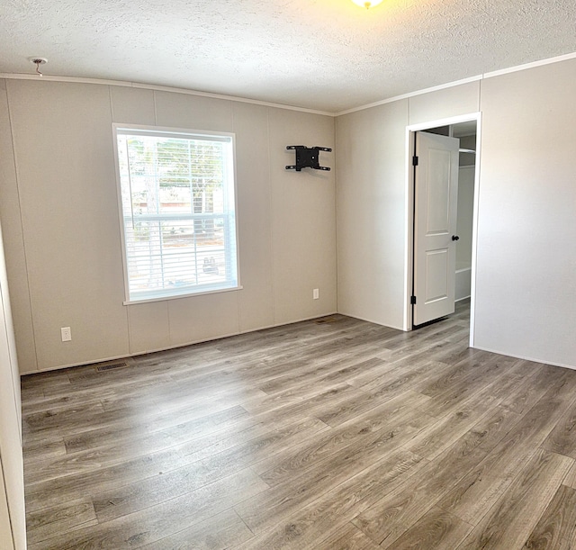 empty room featuring a textured ceiling, ornamental molding, wood finished floors, and visible vents