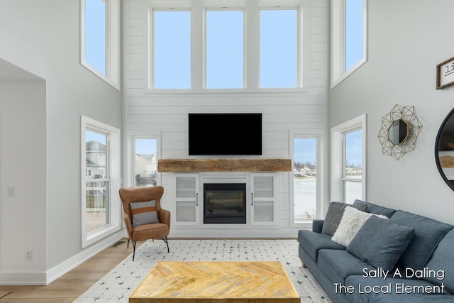 living room with a glass covered fireplace, a high ceiling, baseboards, and wood finished floors