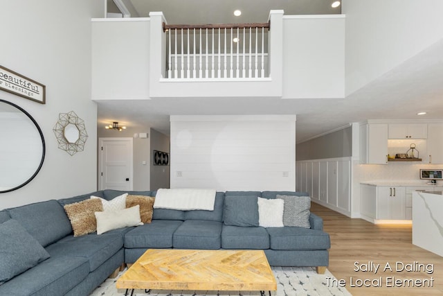 living room featuring ornamental molding, light wood-type flooring, and a high ceiling