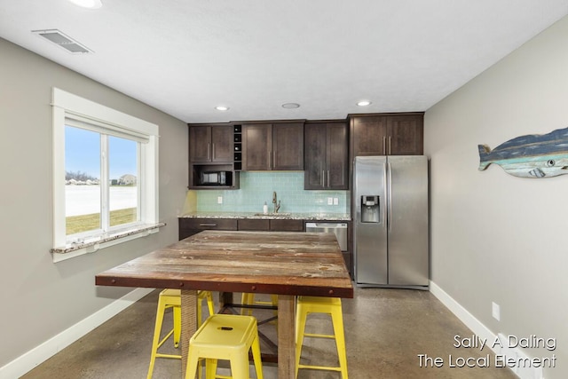 kitchen featuring visible vents, appliances with stainless steel finishes, backsplash, dark brown cabinets, and a sink