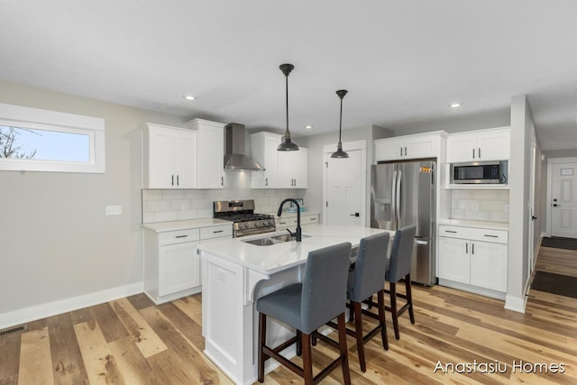 kitchen with a breakfast bar area, a sink, light countertops, wall chimney range hood, and appliances with stainless steel finishes