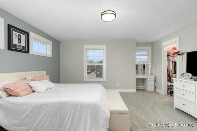 bedroom with light carpet, multiple windows, a walk in closet, and baseboards