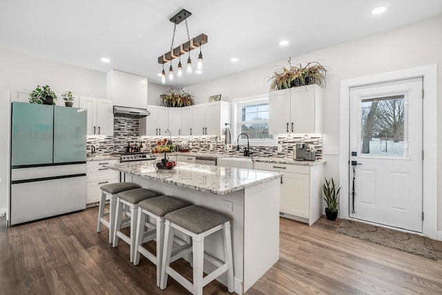 kitchen featuring a breakfast bar, wood finished floors, freestanding refrigerator, ventilation hood, and a sink