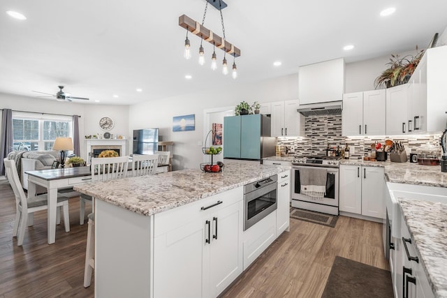 kitchen with a fireplace, stainless steel appliances, backsplash, wood finished floors, and extractor fan