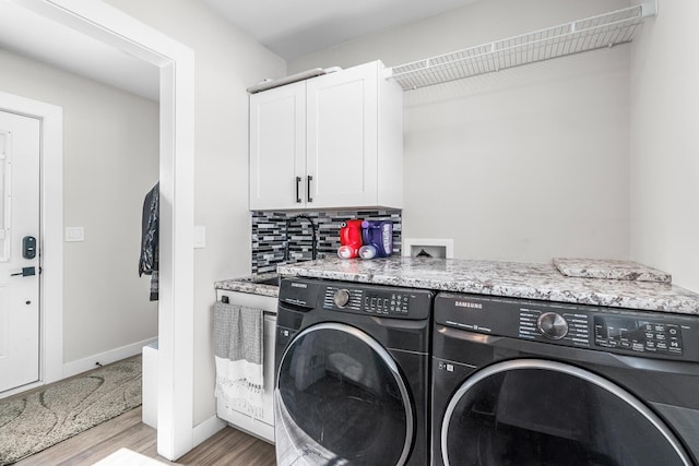 clothes washing area with light wood finished floors, washing machine and dryer, cabinet space, and baseboards