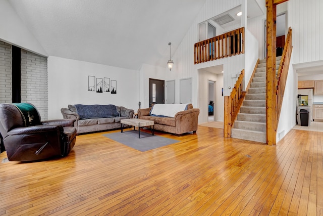 living area featuring light wood finished floors, stairs, and high vaulted ceiling