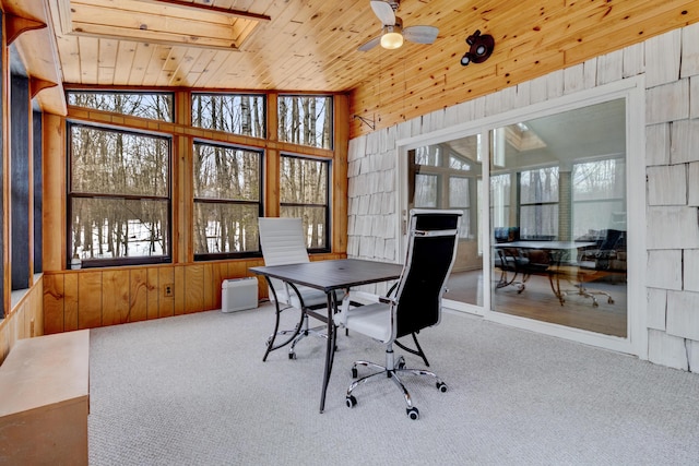 carpeted office space featuring wooden ceiling, ceiling fan, wooden walls, and lofted ceiling with skylight