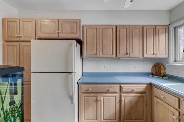 kitchen featuring tasteful backsplash, freestanding refrigerator, light countertops, light brown cabinetry, and a sink