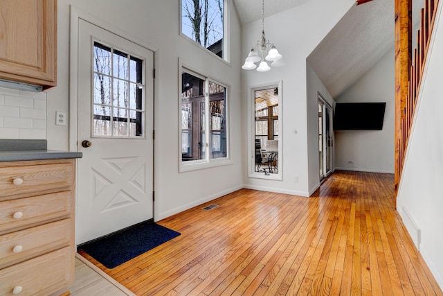 foyer entrance with light wood-style floors, baseboards, visible vents, and a notable chandelier