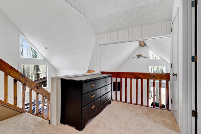 corridor featuring a healthy amount of sunlight, carpet flooring, lofted ceiling with beams, and a textured ceiling