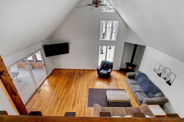 living area featuring a wood stove, a textured ceiling, visible vents, and wood finished floors