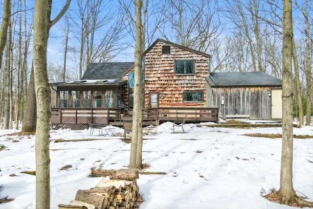 snow covered rear of property with a sunroom and a deck