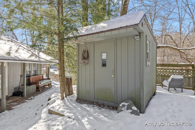 snow covered structure with an outbuilding, a storage shed, and fence