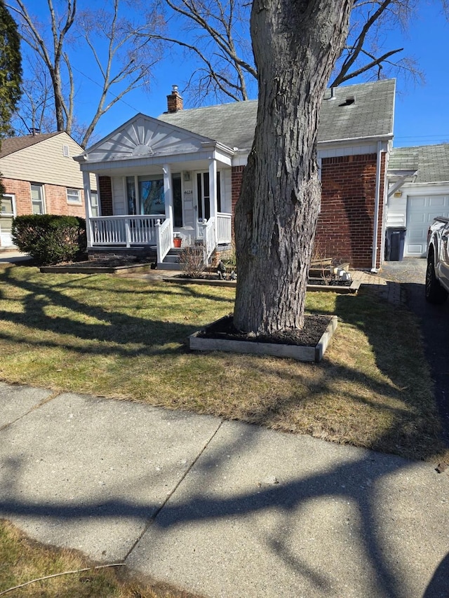 bungalow-style home with a porch, roof with shingles, a front yard, brick siding, and a chimney