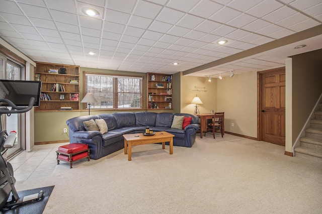 living room featuring light carpet, baseboards, built in shelves, and stairway