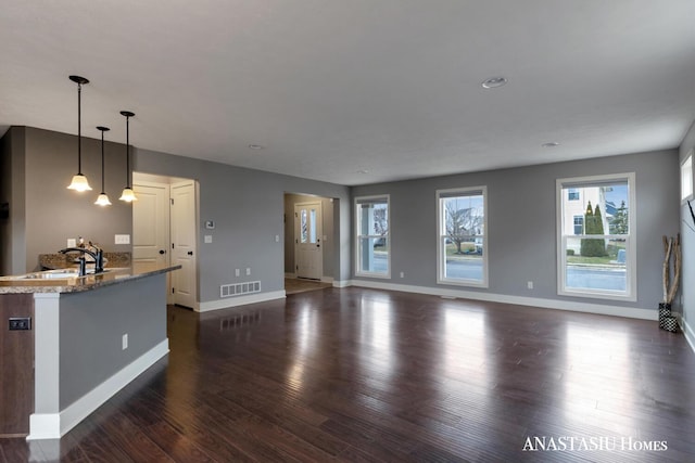 unfurnished living room featuring a chandelier, a sink, visible vents, baseboards, and dark wood-style floors