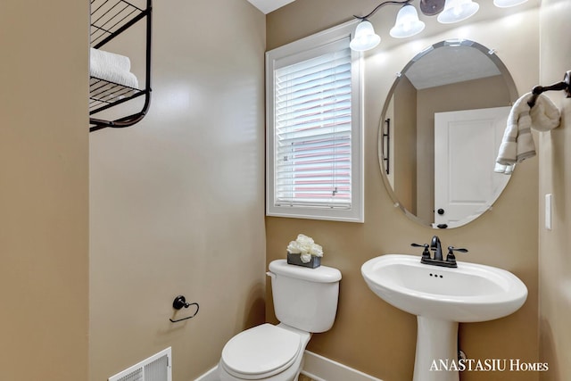 half bathroom with toilet, baseboards, visible vents, and a sink