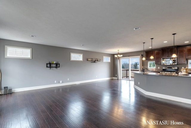 unfurnished living room featuring dark wood-style floors, a chandelier, a sink, and baseboards