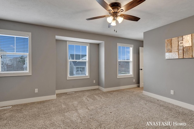 carpeted spare room featuring visible vents, ceiling fan, and baseboards