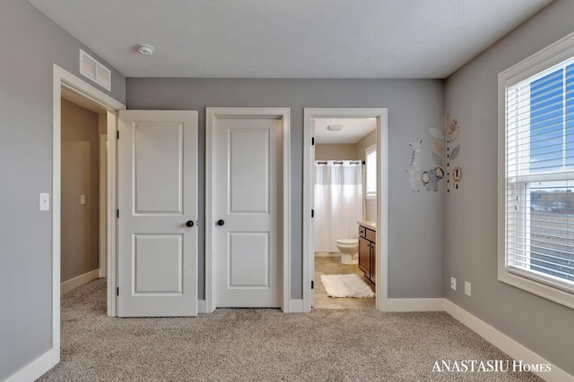 unfurnished bedroom with light carpet, ensuite bathroom, visible vents, and baseboards