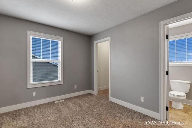 interior space featuring a textured ceiling, connected bathroom, carpet flooring, visible vents, and baseboards