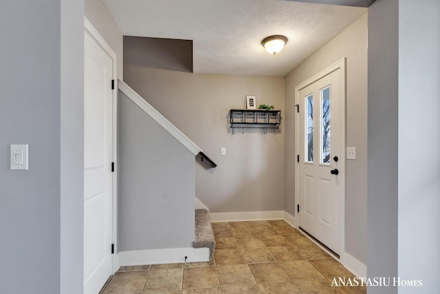 foyer entrance with light tile patterned floors, a textured ceiling, baseboards, and stairs