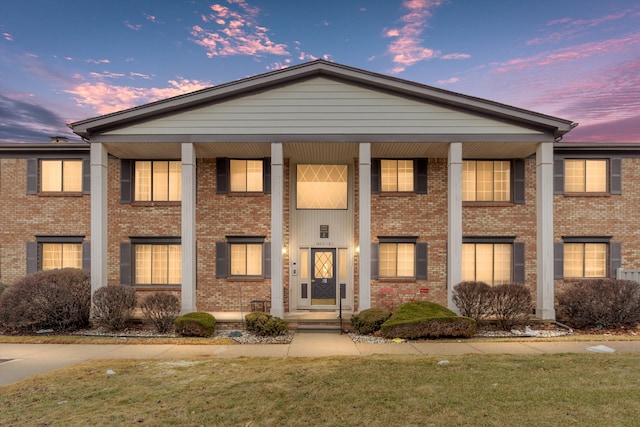 neoclassical home featuring covered porch, brick siding, and a front lawn