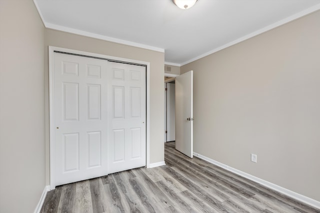 unfurnished bedroom with a closet, crown molding, baseboards, and wood finished floors