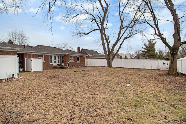 rear view of property with brick siding, a chimney, and a fenced backyard