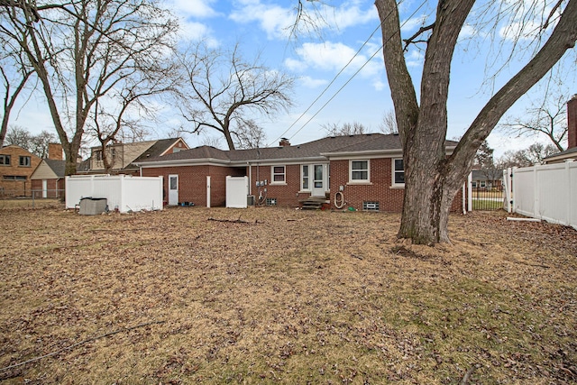 back of property featuring entry steps, a chimney, brick siding, and a fenced backyard