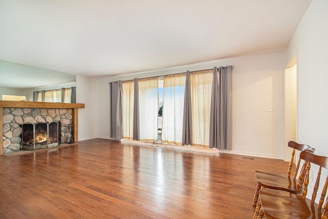 living area with visible vents, a stone fireplace, hardwood / wood-style flooring, and baseboards