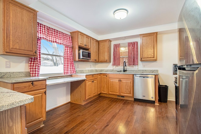 kitchen featuring brown cabinetry, light stone counters, appliances with stainless steel finishes, dark wood-style flooring, and a sink