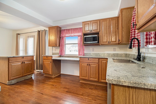 kitchen with dark wood-style floors, stainless steel microwave, brown cabinets, a sink, and built in desk