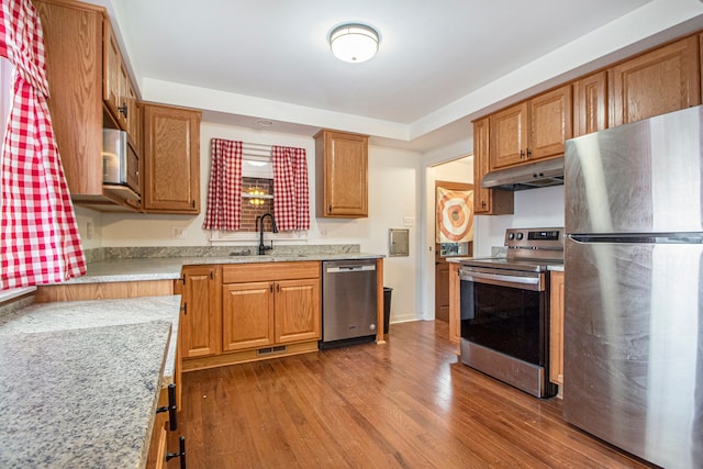 kitchen with under cabinet range hood, stainless steel appliances, dark wood-style flooring, a sink, and visible vents