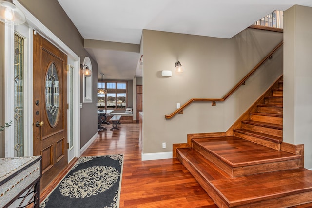 foyer entrance with stairs, wood finished floors, and baseboards