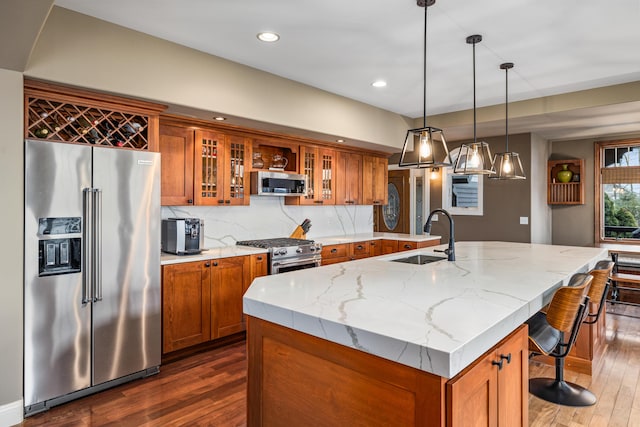 kitchen with appliances with stainless steel finishes, brown cabinetry, a sink, and light stone countertops