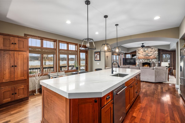 kitchen with arched walkways, dishwasher, dark wood-style flooring, a stone fireplace, and a sink