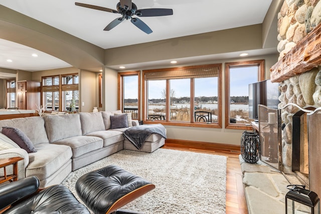 living area featuring light wood-type flooring, ceiling fan, a stone fireplace, and recessed lighting