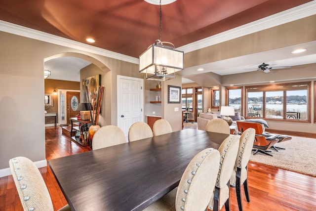 dining area featuring arched walkways, wood-type flooring, crown molding, and baseboards