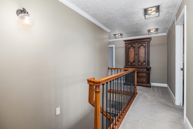 hall with a textured ceiling, carpet flooring, an upstairs landing, baseboards, and ornamental molding