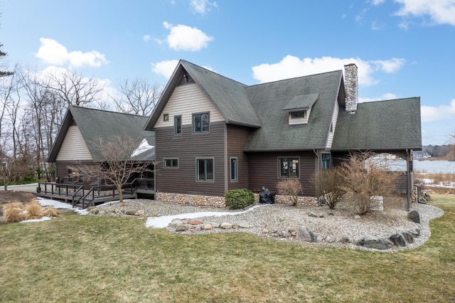 back of property with a deck, a shingled roof, a chimney, and a lawn