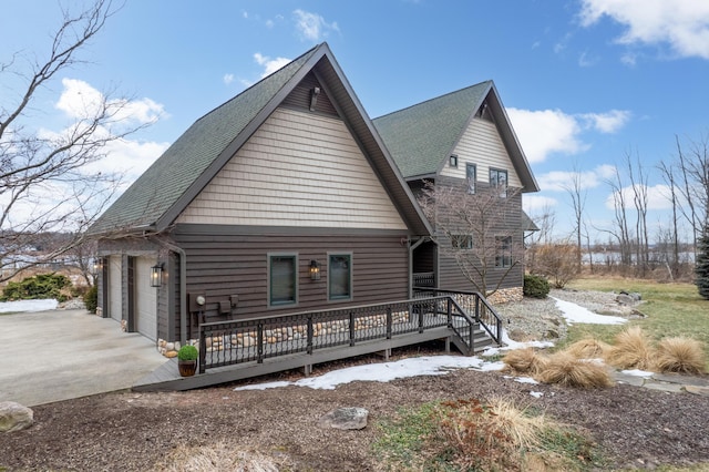 rear view of house featuring driveway, roof with shingles, an attached garage, and a wooden deck