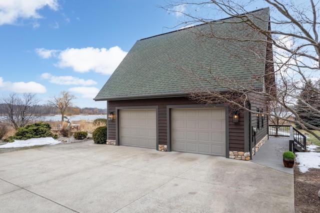 view of side of property featuring a water view, stone siding, a shingled roof, and a garage