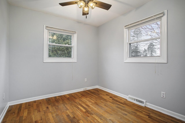 spare room featuring hardwood / wood-style floors, a ceiling fan, visible vents, and baseboards