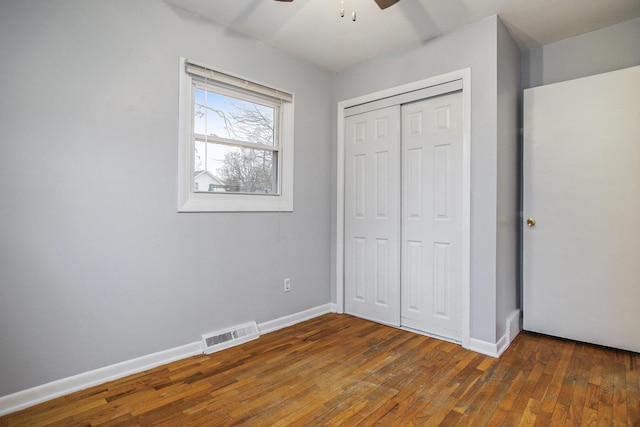 unfurnished bedroom with a closet, wood-type flooring, visible vents, and baseboards